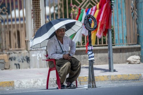 A day-labourer rests at road side as he protects himself from the sun with an umbrella as extreme heat wave threatens the lives of the workers in Erbil, Iraq on July 27, 2023. [Ahsan Mohammed Ahmed Ahmed - Anadolu Agency]