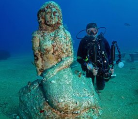 diver poses for a photo with an underwater statue at the Side Underwater Museum, Turkiye's first underwater museum, in Manavgat district of Antalya, Turkiye on June 19, 2023. [Tahsin Ceylan - Anadolu Agency]