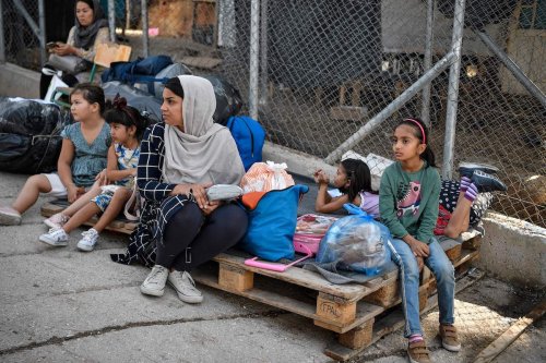 A family of refugees sit on their belongings at the old Samos camp, before being transferred to the new Samos RIC, the first of five new 'closed' migrant camps, on the island of Samos, Greece, on 20 September 2021. [LOUISA GOULIAMAKI/AFP via Getty Images]