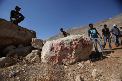 Palestinian Bedouin youths stand near a stone sprayed with graffiti in Hebrew reading, 'administrative revenge', in Ein Samiya, a village in the Israeli-occupied West Bank, on August 13, 2015 [ABBAS MOMANI/AFP via Getty Images]
