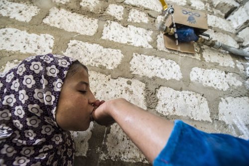 Egyptian mother cups her hands under a running tap in her yard to let her her daughter 6 drink, in the village of al-Jendaya, in the Bani Mazar province, in the Minya governorate some 200km south of Cairo on 5 April 2016. [KHALED DESOUKI/AFP via Getty Images]