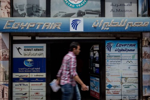 Pedestrians walk past a tour agency promoting flights by EgyptAir in Cairo, Egypt. [Chris McGrath/Getty Images]