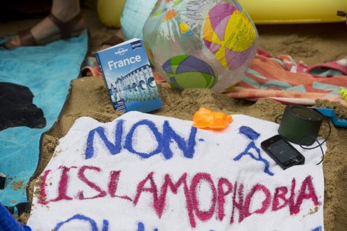 A beach towel reads "No to Islamophobia" written in the colours of the French flag lying in the sand of a 'beach' created by protesters outside the French Embassy in London on August 25, 2016, during a "Wear what you want beach party" to demonstrate against the ban on Burkinis on French beaches and to show solidarity with Muslim women [JUSTIN TALLIS/AFP via Getty Images]